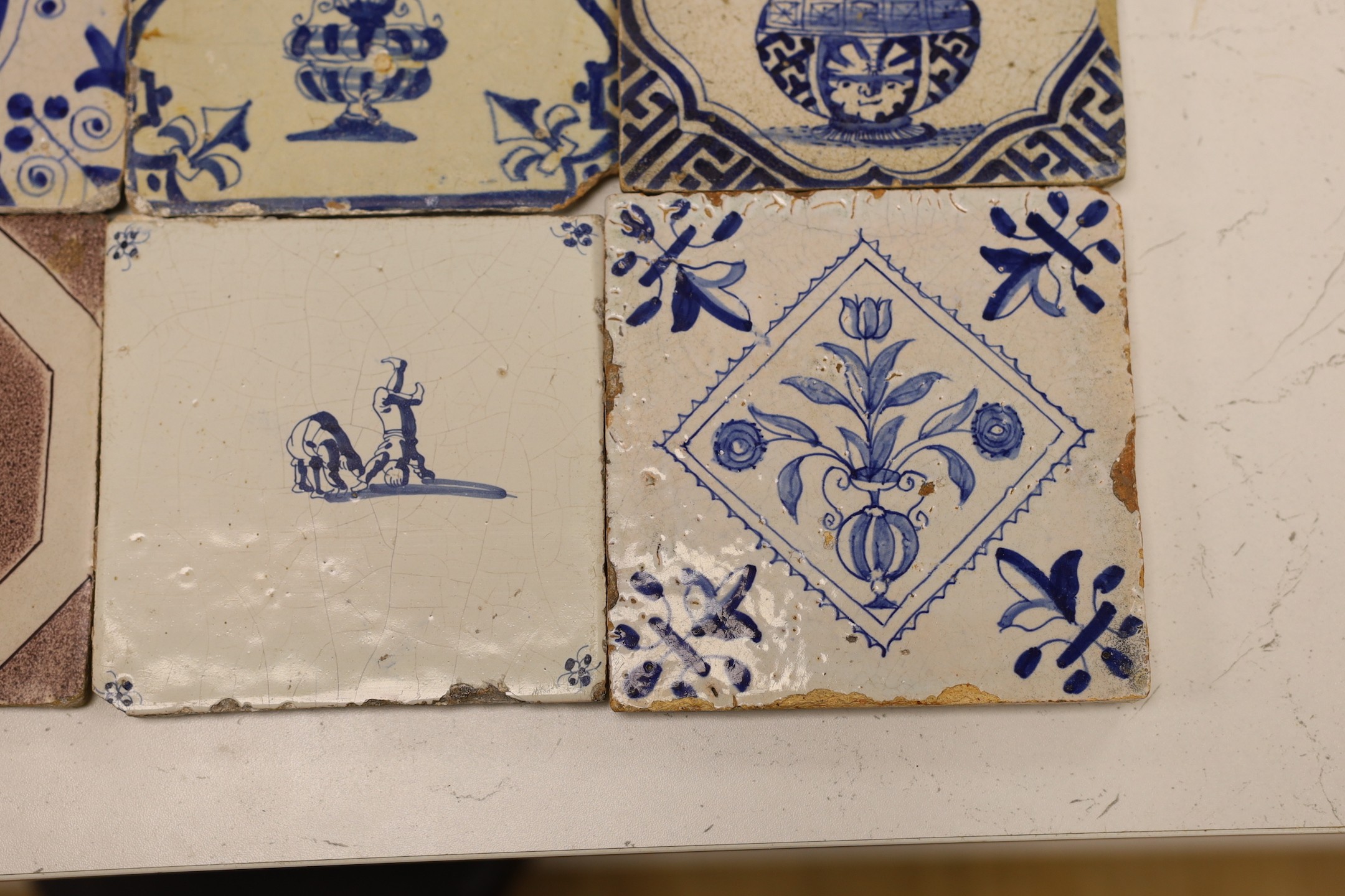 Four mid 17th century Delft blue and white ‘urn of flowers’ tiles, and an 18th century Delft ‘acrobats’ tile and blue and manganese ‘landscape’ tile (6)